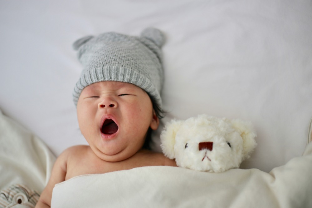 A baby yawning beside a small teddy